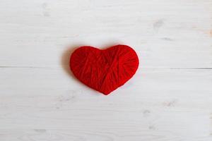 röd hjärta form tillverkad från ull på vit trä- bakgrund foto