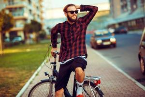 ung man i solglasögon ridning en cykel på stad gata foto