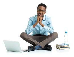 Lycklig afrikansk amerikan högskola studerande med bärbar dator, böcker och flaska av vatten Sammanträde på vit foto
