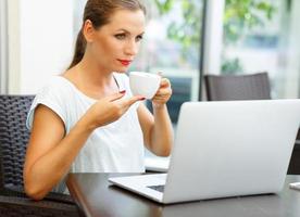 attraktiv företag kvinna Sammanträde i en Kafé med en bärbar dator och drycker henne morgon- kaffe foto