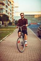 eleganta man i solglasögon ridning en cykel på stad gata foto