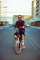 man i solglasögon ridning en cykel på stad gata foto