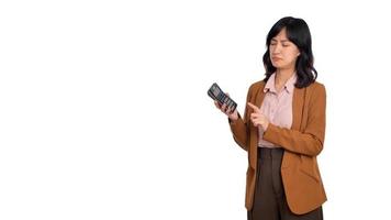 ledsen kontor flicka, asiatisk kvinna tjura och rynkar besviken medan använder sig av en kalkylator, stående upprörd och bedrövad mot vit bakgrund foto