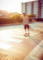 man i solglasögon med en skateboard på en gata i de stad på solnedgång ljus foto