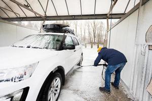 man tvättning hög tryck vatten amerikan sUV bil med tak kuggstång på själv service tvätta i kall väder. foto