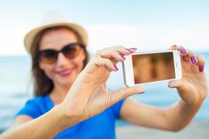 flicka i de hatt framställning selfie förbi de smartphone på de bakgrund av hav kust, adriatisk hav foto