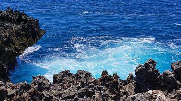 de turkos blå hav är bruten förbi vulkanisk rocks. foto