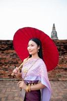 skön thai flicka i traditionell klänning kostym röd paraply som thai tempel var är de offentlig plats, thai kvinna i traditionell kostym av thailand. foto