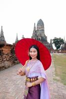 skön thai flicka i traditionell klänning kostym röd paraply som thai tempel var är de offentlig plats, thai kvinna i traditionell kostym av thailand. foto