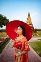 skön thai flicka i traditionell klänning kostym röd paraply som thai tempel var är de offentlig plats, thai kvinna i traditionell kostym av thailand. foto