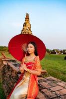 skön thai flicka i traditionell klänning kostym röd paraply som thai tempel var är de offentlig plats, thai kvinna i traditionell kostym av thailand. foto