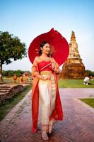 skön thai flicka i traditionell klänning kostym röd paraply som thai tempel var är de offentlig plats, thai kvinna i traditionell kostym av thailand. foto