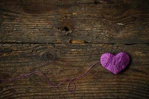 lila hjärta med en boll av tråd på på gammal sjaskig trä- bakgrund foto