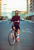 ung man i solglasögon ridning en cykel på stad gata foto