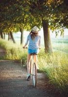 härlig ung kvinna i en hatt ridning en cykel utomhus. aktiva människor foto