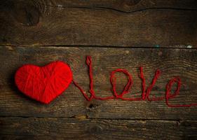 röd hjärta form med ett inskrift kärlek tillverkad från ull på gammal sjaskig trä- bakgrund foto