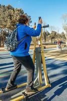 en pensionerad kvinna med en ryggsäck på henne axlar på ett aktiva promenad utomhus är engagerad i övning Utrustning i de parkera. senior kvinna tar vård av henne hälsa foto