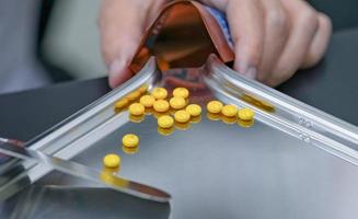 selektiv fokus på gul tabletter piller på rostfri bricka med fläck hand av apotekare eller apotek tekniker räkning piller in i en plast dragkedja väska. recept medicin. medicinsk hälsa vård. foto