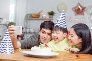 Lycklig födelsedag fest i familj, asiatisk ung förälder far, mor och liten söt pojke eller barn firar, använder sig av smart telefon selfie, ta Foto och video ring upp under firande tillsammans på Hem.