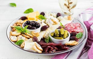 antipasto tallrik med basturma, salami, blå ost, nötter, ättiksgurka och oliver på en vit trä- bakgrund. foto