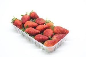 jordgubbar i en plastbehållare på en vit bakgrund foto