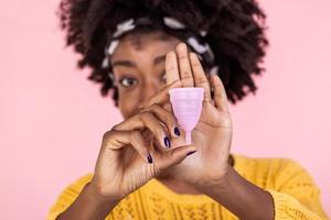 stänga upp porträtt av afrikansk amerikan kvinna innehav menstruations- kopp isolerat över lila studio bakgrund, Lycklig kvinna, har period, motvilja till använda sig av bindor eller tamponger foto