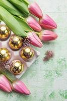 hållare med påsk ägg målad gyllene färger och rosa tulpaner på en grön trä- bakgrund. foto