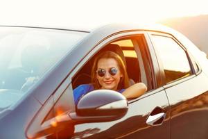 leende kvinna körning en bil på solnedgång foto