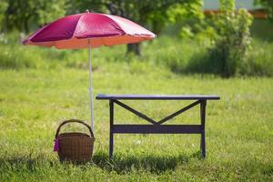 för en picknick. på en grön äng där är en trä- tabell, en korg- korg och zoner från de Sol. foto