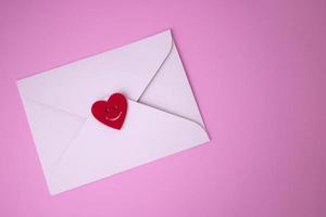 vit kuvert med röd hjärtan för hjärtans dag på en rosa bakgrund. de begrepp av en kärlek meddelande för Mars 8, mors dag, fars dag, familj dag foto