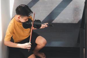 ett litet asiatiskt barn som spelar och tränar violinmusikaliskt stränginstrument mot i hemmet, koncept för musikalisk utbildning, inspiration, tonåring konstskola student. foto