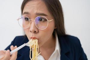 upptagen och trött affärskvinna äter spaghetti för lunch på de skrivbord kontor och arbetssätt till leverera finansiell uttalanden till en chef. överarbetad och ohälsosam för redo måltider, burnout begrepp. foto