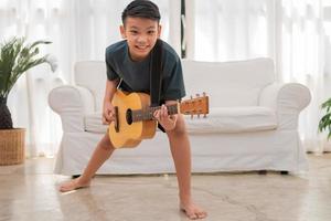 porträtt av en asiatisk Lycklig leende pojke har roligt spelar gitarr musik begrepp, barn musik skola. sten konsert, musik för barn och småbarn begrepp foto