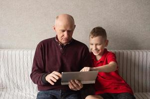 söt pojke lär morfar till skriva meddelanden på en läsplatta foto