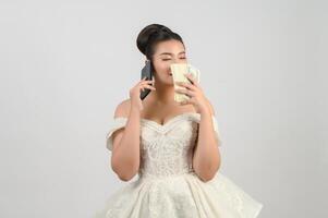 ung asiatisk skön brud inlägg med smartphone och sedel i hand foto