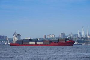 marinmålning med ett rött containerfartyg och stadssilhuett i bakgrunden i Vladivostok, Ryssland foto