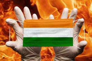 läkare innehav i vit handskar skydd medicinsk ansikte mask, respiratorisk bandage med Indien nationell Land flagga överlagrad på mask. begrepp foto