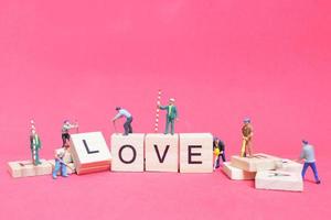 miniatyrarbetare samarbetar för att bygga ordet kärlek på träklossar med rosa bakgrund, alla hjärtans dagskoncept