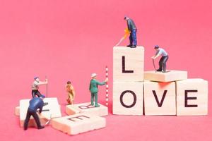 miniatyrarbetare samarbetar för att bygga ordet kärlek på träklossar med rosa bakgrund, alla hjärtans dagskoncept