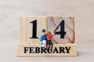 miniatyrpar med träklossar 14 februari text på trä bakgrund, glad Alla hjärtans dag koncept foto