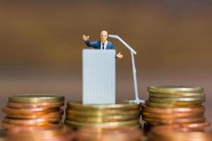 miniatyr affärsman talar på ett podium på en stapel mynt, affärs- och finansiella investeringskoncept foto