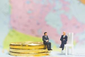 miniatyraffärsmän på en stapel mynt med en världskarta i bakgrunden, pengar och ekonomisk framgångsidé foto