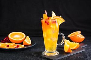 orange tranbär brusande cocktail i en glas och frukt Nästa till den på en mörk bakgrund. hemlagad mocktail foto