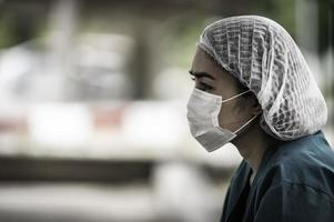 trött deprimerad kvinnlig asiatisk skrubbsköterska bär ansiktsmask blå uniform sitter på sjukhusgolvet, ung kvinna läkare stressad av hårt arbete foto