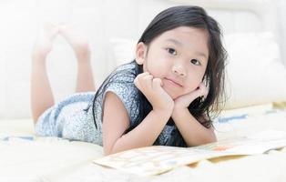 söt liten asiatisk flicka i nattlinne läsning en bok foto