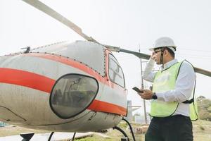 asiatisk man aero ingenjör arbetssätt på helikopter i hangar ser på digital läsplatta foto