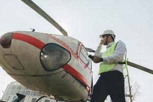 asiatisk man aero ingenjör arbetssätt på helikopter i hangar ser på digital läsplatta foto