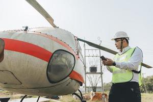 asiatisk man aero ingenjör arbetssätt på helikopter i hangar ser på digital läsplatta foto