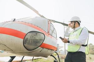 asiatisk man aero ingenjör arbetssätt på helikopter i hangar ser på digital läsplatta foto
