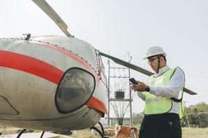 asiatisk man aero ingenjör arbetssätt på helikopter i hangar ser på digital läsplatta foto